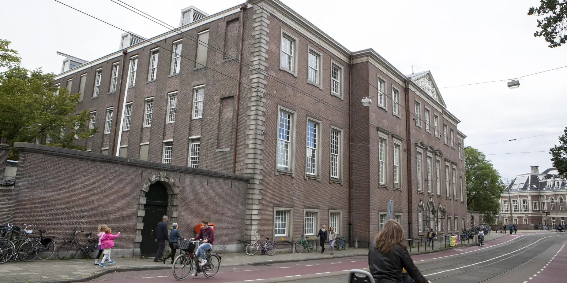 Het Sarphatihuis in Amsterdam, een bakstenen gebouw van vier verdiepingen langs de straat met fietsers en voorbijgangers