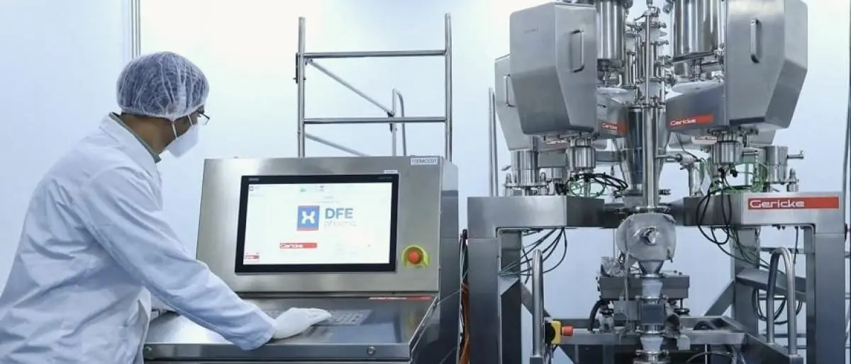 Een technicus in cleanroomkleding aan een bedieningsconsole naast een roestvrijstalen procesinstallatie