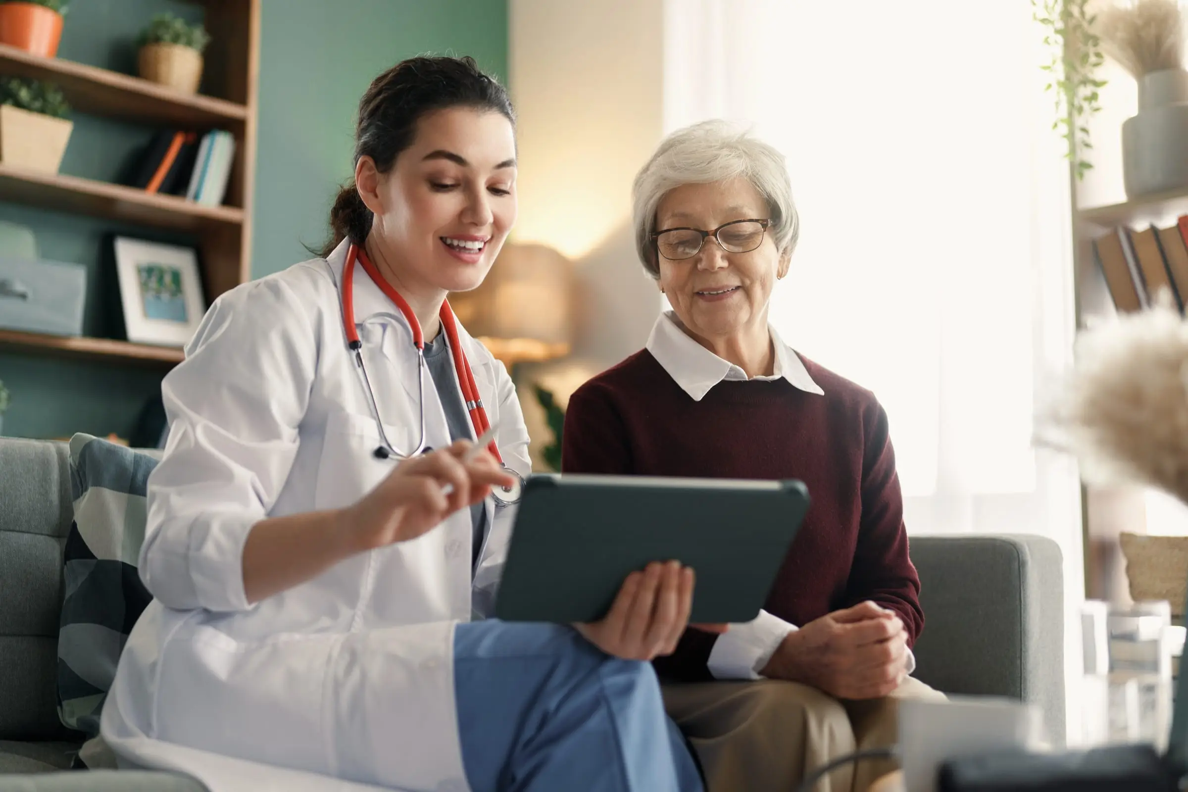 Een zorgverlener laat een oudere vrouw iets zien op een tablet in haar woonkamer